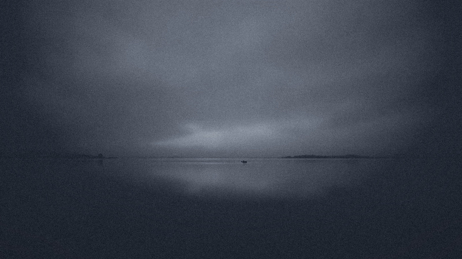 Still water at blue hour under a slate sky; a thin bright horizon.